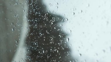 Snow fall on window and melting into water drops on glass in the forest. Large rain drops strike window during winter shower. Pure rain drops. Vertical