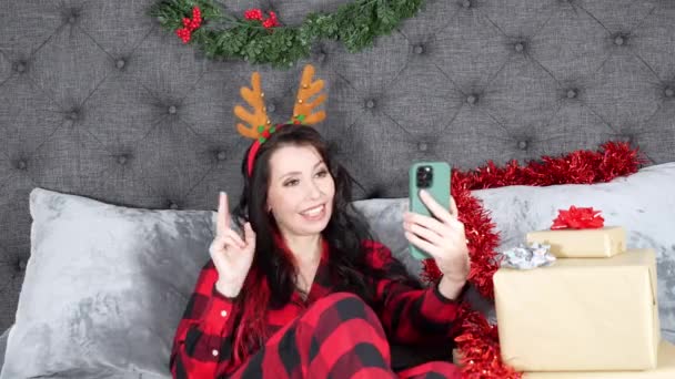 アントラのヘッドバンドを着て赤い平野の若い美しい女性 プレゼント付きのクリスマスの装飾された部屋で電話で友人と話す — ストック動画