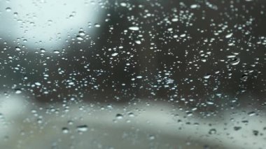 Snow fall on window and melting into water drops on glass in the forest. Large rain drops strike window during winter shower. Pure rain drops