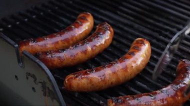 Izgara barbekü sosisleri paslanmaz ızgarada ve alevler yakın. Yiyecek ve mutfak konsepti