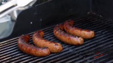 Izgara barbekü sosisleri paslanmaz ızgarada ve alevler yakın. Yiyecek ve mutfak konsepti