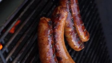 Izgara barbekü sosisleri paslanmaz ızgarada ve alevler yakın. Yiyecek ve mutfak konsepti