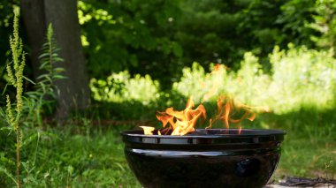 Black round Barbecue Grill with Fire on Open Air with green grass. Fire Flame. Prepairing charcoal for the grilling bbq outdoors