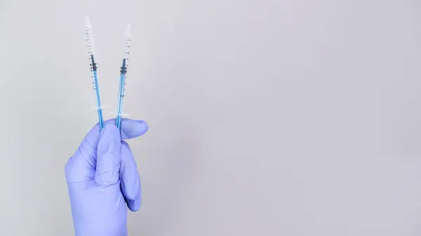Hand in blue gloves of doctor or nurse holding syringe with liquid vaccine over grey background with copy space. New vaccine. Unknown vaccine. Medical gloves