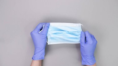Doktor ya da hemşirenin gri arka planda koruyucu mavi maske taktığı mavi eldivenleri fotokopi alanı ile birlikte teslim edin. Yeni bir aşı. Bilinmeyen aşı. Tıbbi eldivenler