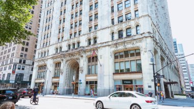 Değişik araçlar, büyüleyici binalar, yeşil ağaçlar ve kentsel yaşamın enerjik özünü özetleyen canlı bir atmosferle dolu hareketli bir New York caddesi..