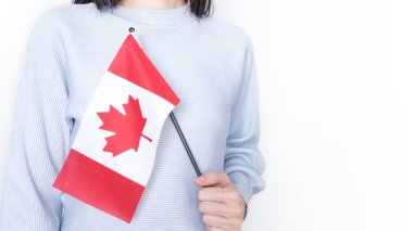 Gri arka planda küçük Kanada bayrağı taşıyan beyaz tişörtlü tanınmamış kız çocuğu, Kanada günü, tatil, oy, göç, vergi, kopya alanı.