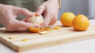 Masadaki kesme tahtasının üzerinde portakal kabuğu soyulmuş eller, Noel 'de yemek yapmak için bir sürü sulu taze meyve..