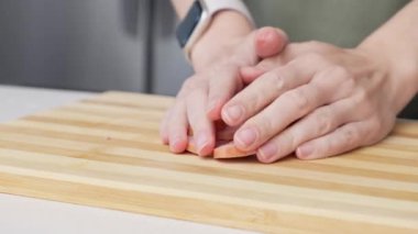 Mutfak ortamında farklı malzemelerle ahşap bir kesme tahtasından kesilmiş sosis alan bir kadının yakın çekimi.