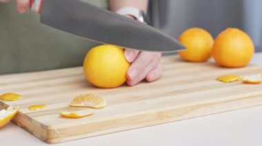 Masadaki kesme tahtasının üzerinde portakal renginde mandalina kesen eller, Noel 'de pişirmek için bir sürü sulu taze meyve..