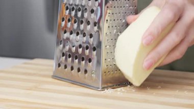 Ahşap tahtanın üzerinde çelik rendesi olan geleneksel parmesan peynirini rendeleyen şefin yavaş hareketi..