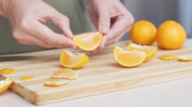 Masadaki kesme tahtasının üzerinde portakal renginde mandalina kesen eller, yemek yapmak için bir sürü sulu taze meyve..