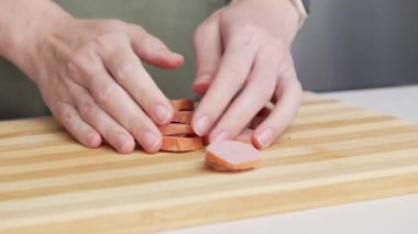 Mutfak ortamında farklı malzemelerle ahşap bir kesme tahtasından kesilmiş sosis alan bir kadının yakın çekimi.