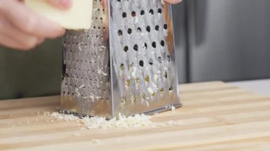 Ahşap tahtanın üzerinde çelik rendesi olan geleneksel parmesan peynirini rendeleyen şefin yavaş hareketi..