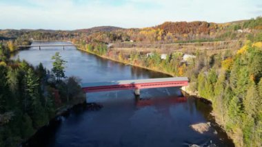 Güneşli bir sonbahar gününde güzel kırmızı köprünün ve gölün pürüzsüz yeşil sularının havadan görünüşü. Ormanlar ve evlerle çevrili zümrüt göl manzaralı kuşların bakış açısı