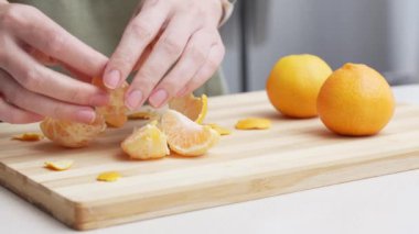 Masadaki kesme tahtasının üzerinde portakal kabuğu soyulmuş eller, Noel 'de yemek yapmak için bir sürü sulu taze meyve..