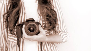 Elinde DSR kamerası olan bir fotoğrafçı. Otoportre, ön manzara. Yılın Rengi Mocha Mousse. Yüzsüz, kızıl saçlı, tişörtlü, elinde fotoğraf makinesi olan hoş bir kadın. Beyaz arka plan.