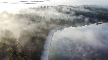 Görüntü, sabahları çok güzel bir göl kenarı kamp alanını gösteriyor. Kamp alanı yemyeşil ağaçlarla çevrili ve göl ince bir sis tabakasıyla örtülmüş. Huzurlu ve sakin bir atmosfer yaratıyor..