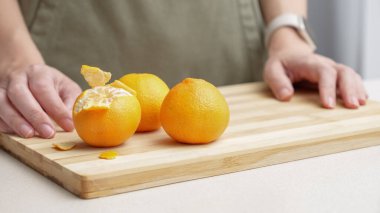 Masadaki kesme tahtasının üzerinde portakal kabuğu soyulmuş eller, Noel 'de yemek yapmak için bir sürü sulu taze meyve..