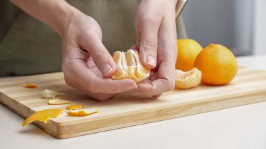 Masadaki kesme tahtasının üzerinde portakal kabuğu soyulmuş eller, Noel 'de yemek yapmak için bir sürü sulu taze meyve..