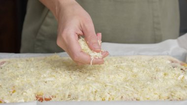 Izgara peynir, aşçının elinden pizzanın üzerine düşer. Ev yapımı pizza. Pizza için rendelenmiş peynir.