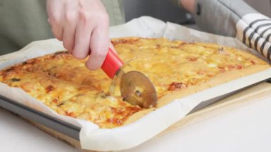 Yuvarlak bir bıçakla pizza kesmek. Lezzetli pizzanın parçalara ayrıldığı yakın plan çekimler. Yavaş çekimde bir pizzayı kesiciyle birden fazla dilime ayırmak.