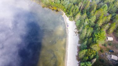 Görüntü, sabahları çok güzel bir göl kenarı kamp alanını gösteriyor. Kamp alanı yemyeşil ağaçlarla çevrili ve göl ince bir sis tabakasıyla örtülmüş. Huzurlu ve sakin bir atmosfer yaratıyor..