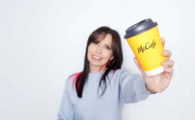 Uzun siyah saçlı neşeli kadın elinde McDonalds sarısı kahve fincanı beyaz arka planda neşe içinde Ottawa on Canada 2024-10-28