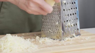 Ahşap tahtanın üzerinde çelik rendesi olan geleneksel parmesan peynirini rendeleyen şefin yavaş hareketi..