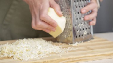 Ahşap tahtada çelik rendesi olan geleneksel mozzarella peynirini rendeleyen şef..