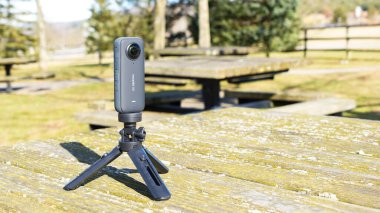 Siyah Tripod ve Insta360 kamera açık hava parkındaki bir masada konumlanmış. Syracuse NY USA - 08.02.2024.