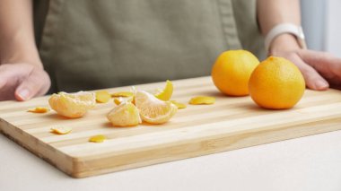 Masadaki kesme tahtasının üzerinde portakal kabuğu soyulmuş eller, Noel 'de yemek yapmak için bir sürü sulu taze meyve..