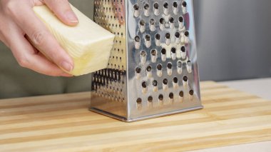 Ahşap tahtada çelik rendesi olan geleneksel parmesan peynirini rendeleyen şef..