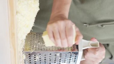 Ahşap tahtanın üzerinde çelik rendesi olan geleneksel parmesan peynirini rendeleyen şefin yavaş hareketi..