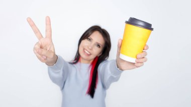 Sarı bir kahve fincanı tutan gülümseyen bir kadın. Üzerinde beyaz bir arka plan var..