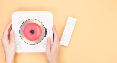 Görüntü şeftali arkaplanda dinlenen uzaktan kumandalı beyaz bir CD çalar gösteriyor. CD çaların içinde canlı kırmızı bir CD var. Modern tasarım ve işlevselliğini gösteriyor..