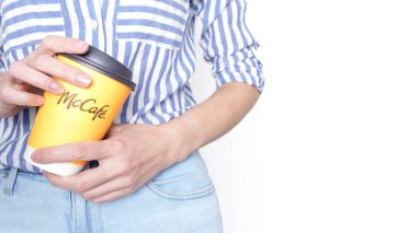 Mavi kot pantolon ve mavi çizgili gömlek giyen sarı bir McCafe kahve fincanı tutan kadın. Ottawa Kanada 'da 06-17-2024.