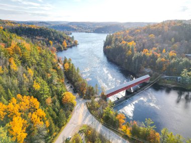 Resim, güzel bir sonbahar ormanında nehrin üzerindeki küçük kırmızı bir köprüyü gösteriyor. Ağaçlar tam yapraklı ve yapraklar sarıya, turuncuya ve kırmızıya dönüyor. Su sakin ve berrak..