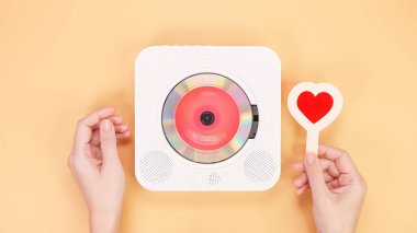 A vintage white retro styled portable compact disc player sits next to a vibrant red heart-shaped object, beautifully isolated on a soft peach background, creating a nostalgic and romantic atmosphere. clipart