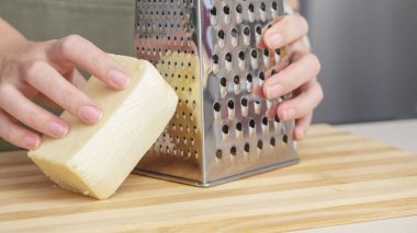 Ahşap tahtada çelik rendesi olan geleneksel parmesan peynirini rendeleyen şef..