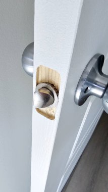 Hasarlı bir kapı mandalının yakın çekimi, açıktaki ahşap çerçeveyi ortaya çıkarıyor, bir ev onarım projesini vurguluyor. Bu resim, arızalı bir kapı mandalı için gereken iç düzeltmeyi gösterir.