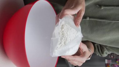 Bir insan mutfakta kırmızı bir karıştırma kabının üzerinde bir torba un tutar. Sahne, pasta pişirme, hazırlık ve malzemelerin ön adımlarını yakalıyor.