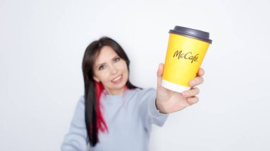 Ottawa On Canada - 2024-10-28: Uzun siyah saçlı neşeli kadın beyaz arka planda neşeli bir şekilde McDonalds sarı kahve fincanını tutuyor.