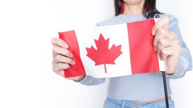 Gri arka planda küçük Kanada bayrağı taşıyan beyaz tişörtlü tanınmamış kız çocuğu, Kanada günü, tatil, oy, göç, vergi, kopya alanı.