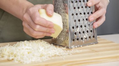 Ahşap tahtada çelik rendesi olan geleneksel mozzarella peynirini rendeleyen şef..