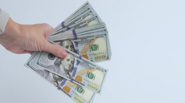 Birkaç yüz dolarlık banknotları tutan bir el. Banknotlar düzgünce düzenlenmiş, mavi ve yeşil renkler sergileniyor. Arkaplan düz beyaz.