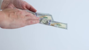 Eller, beyaz arka planda 100 dolarlık banknotlarla para yağdırır. Sahne mali işlemleri ve para işleme örneklerini gösteriyor.