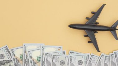 Sarı arka planda bir yığın Amerikan doları var. Uçak dolarların üzerinde hareket ediyor. Seyahat masrafları, finans, zenginlik