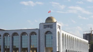 Bişkek, Kırgızistan - 09.15.2024: Ilbirs Mimari yapısı geniş kemerli pencereler ve altın bir kubbeye sahip, modern tasarımı bulutlu açık mavi gökyüzüne karşı yansıtan