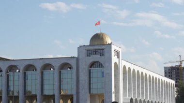 Bişkek, Kırgızistan - 09.15.2024: Ilbirs Mimari yapısı geniş kemerli pencereler ve altın bir kubbeye sahip, modern tasarımı bulutlu açık mavi gökyüzüne karşı yansıtan